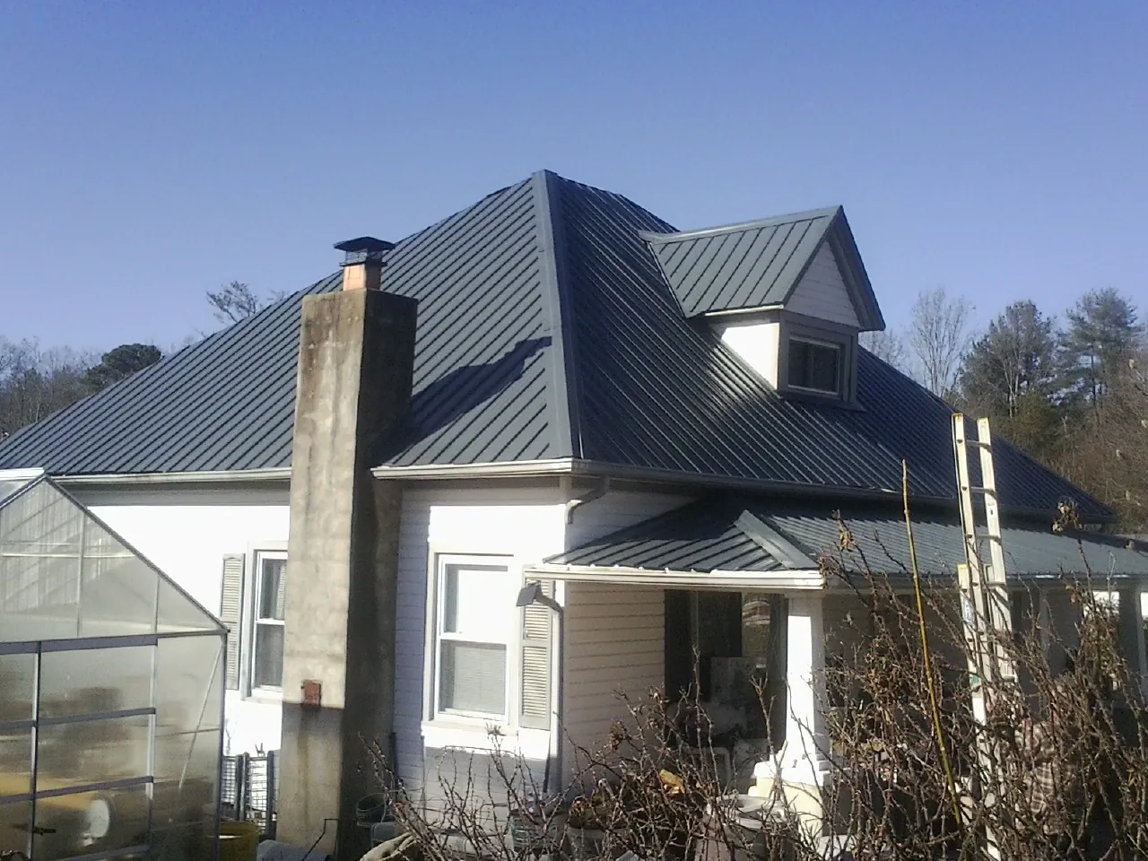 Dark blue standing seam metal roof on a white farmhouse with dormer — Slate & Tile Roof Repair by Roofing Brothers in Burgaw
