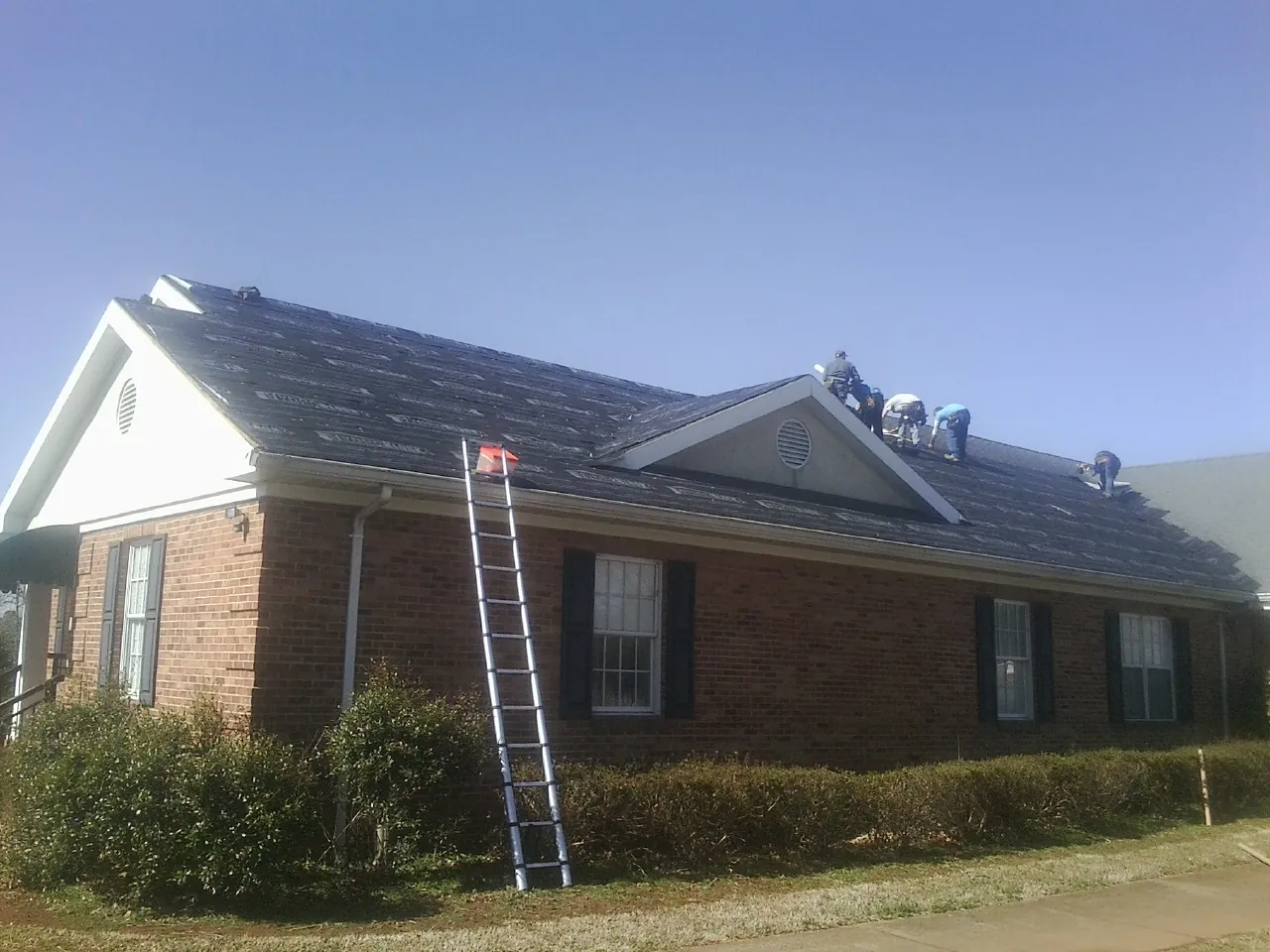 Crew tearing shingles off a brick ranch roof with a ladder set — Metal Roof Repair work by our crew in Burgaw