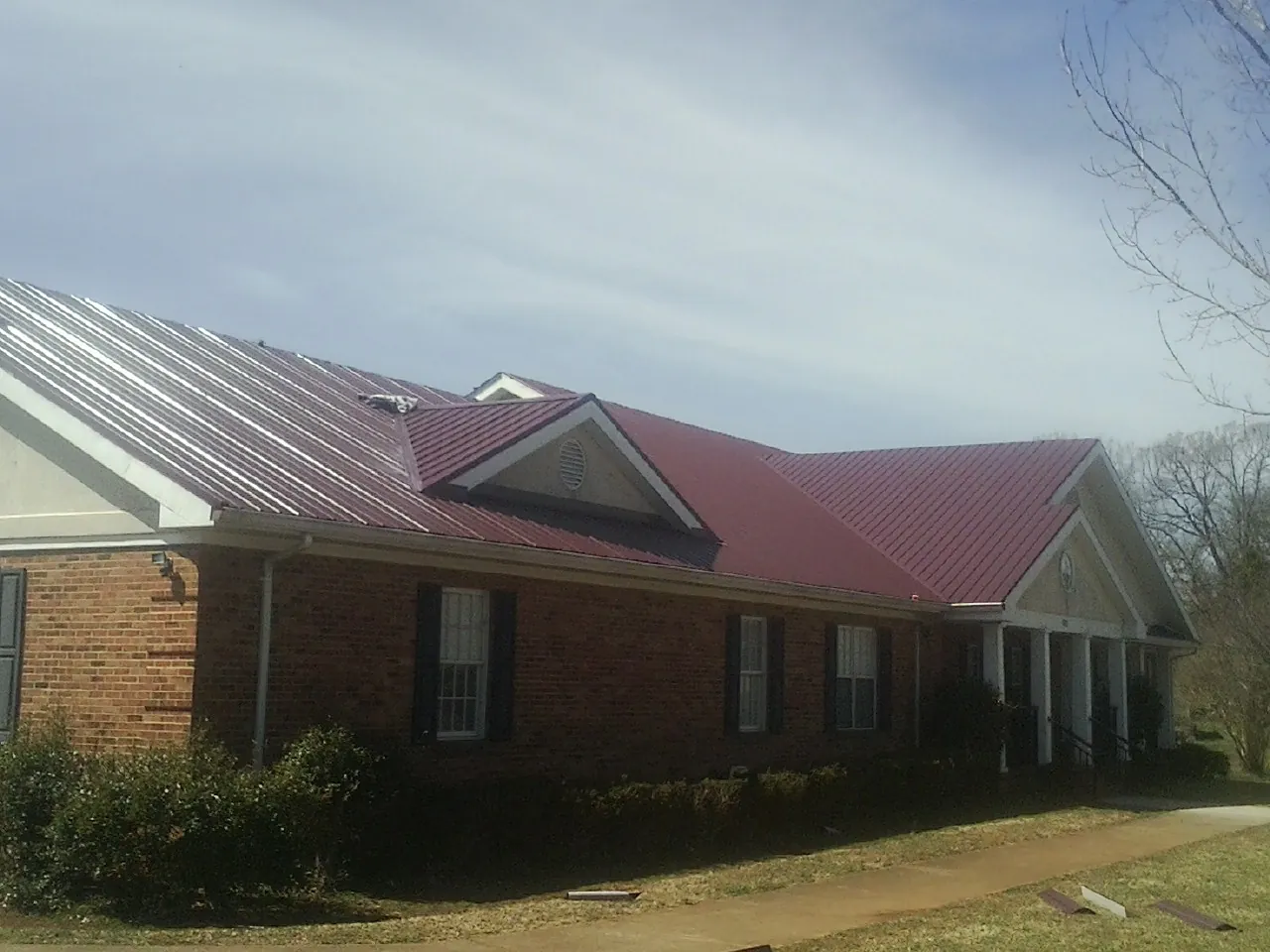 Red metal roof with gabled entries on a long brick building, from a Hail Damage Roof Repair job in Burgaw
