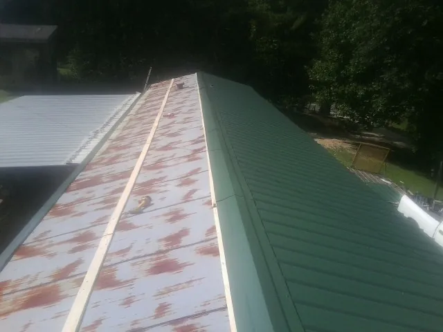 Old rusted panels beside newly installed green metal roofing — Wind Damage Roof Repair by Roofing Brothers in Burgaw