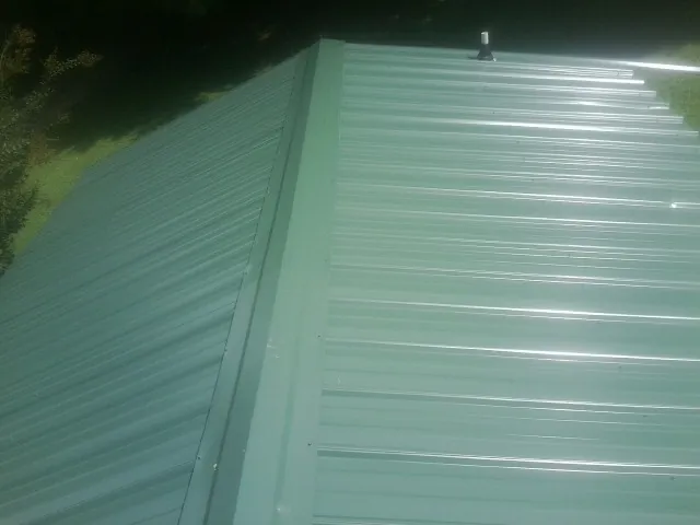 New green metal panels meeting at the ridge of a roof — Flat Roof Repair work by our crew in Burgaw