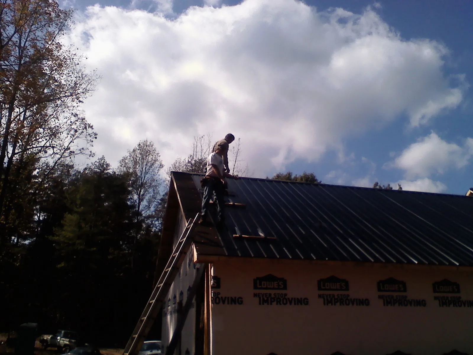 Roofer fastening dark metal panels high against a cloudy sky, from a Roof Inspection job in Burgaw