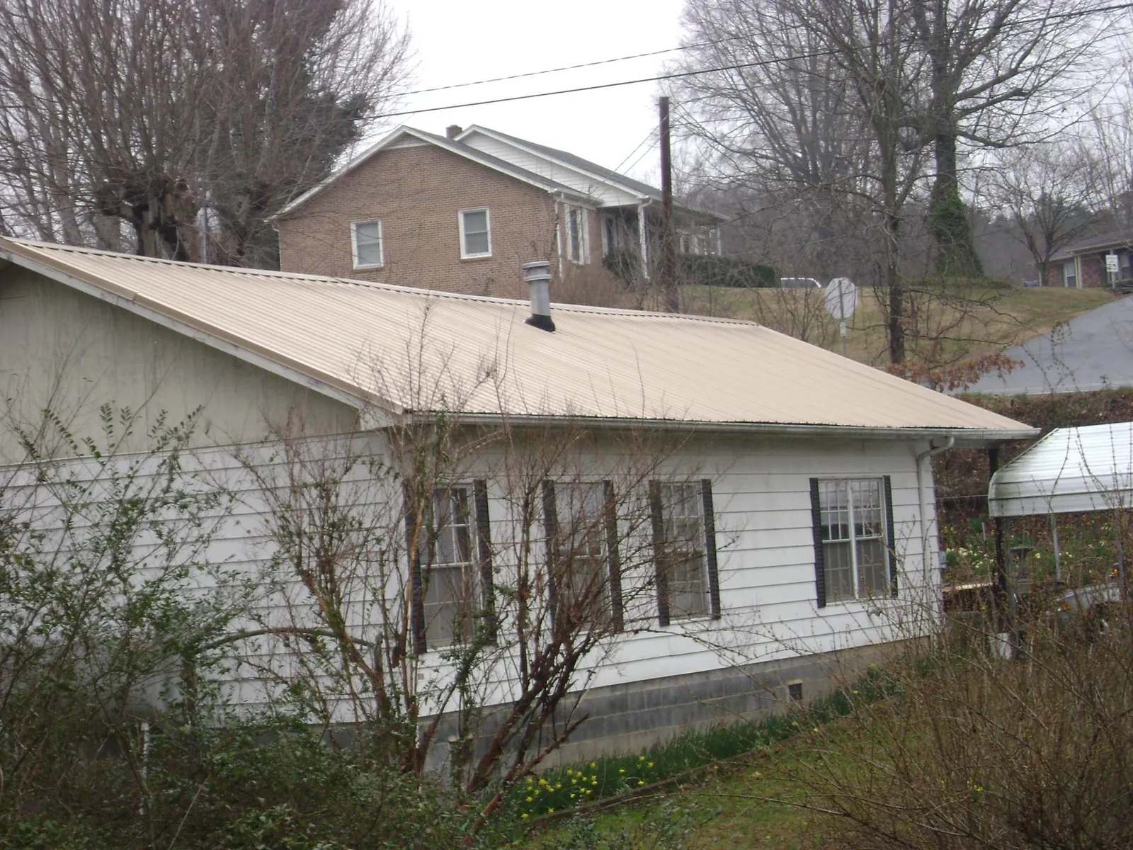 Tan metal roof on a white sided house set into a hillside — Commercial Roofing by Roofing Brothers in Burgaw