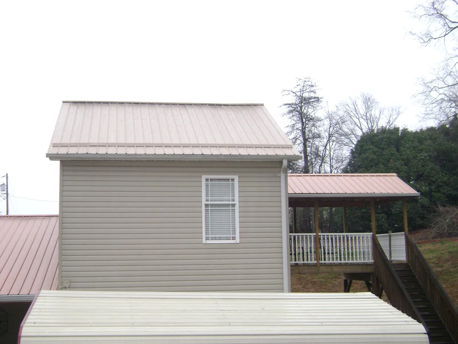 Tan metal roofs on a two story addition and attached porch, from a Roof Replacement job in Burgaw