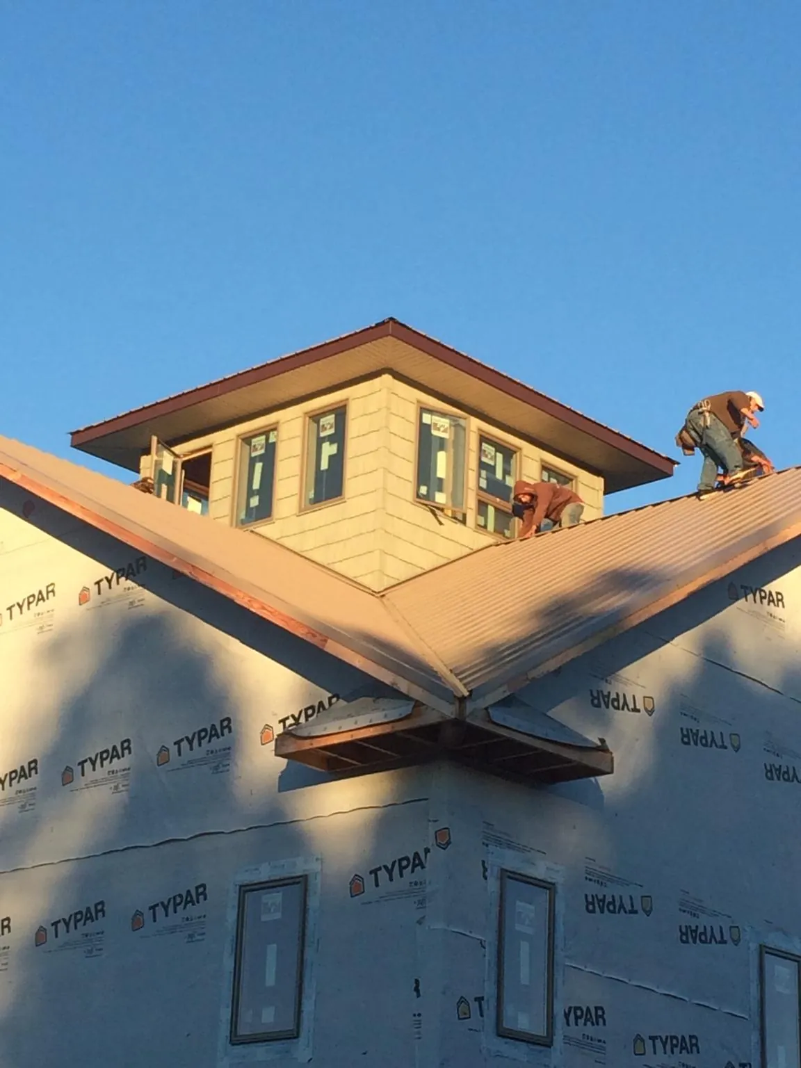 Roofers working around a rooftop cupola on a new metal roof at sunset — Roof Waterproofing in Burgaw by Roofing Brothers